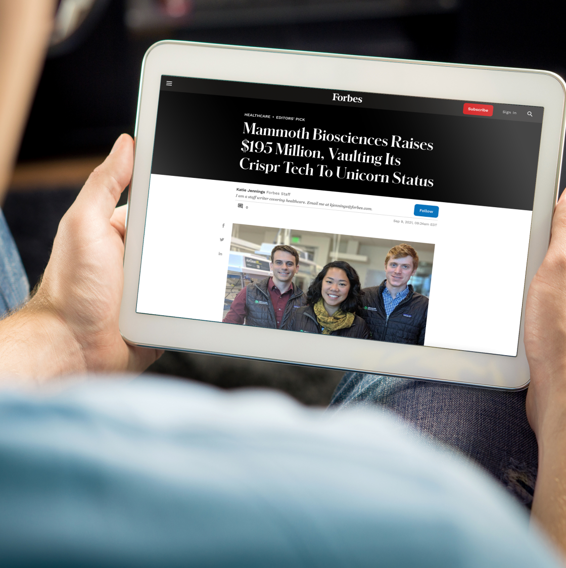 A person holds a tablet. The screen features a Forbes article about Mammoth's CRISPR technology.