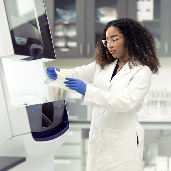 A woman in a lab coat stands at a laboratory machine.