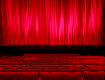 A photo of a classic theater stage with red seats and curtains.