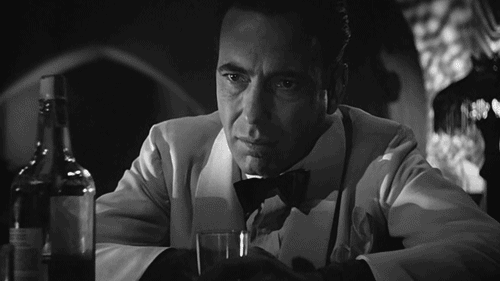 A GIF of actor Humphrey Bogart sitting at a bar, putting his hand over his face.