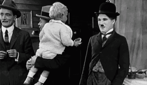 A GIF of Charlie Chaplin making eating a piece of food being held by a small child.