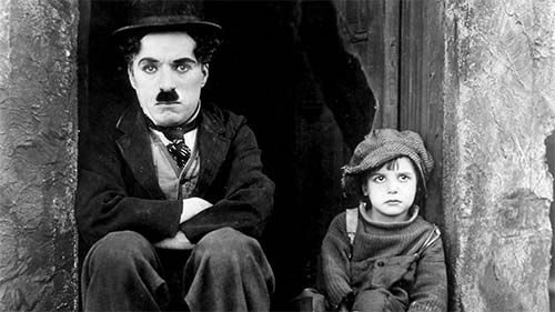 A movie still of Charlie Chaplin sitting next to a child.