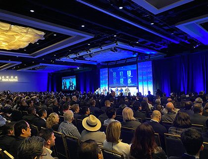 A crowd of people gather to listen to a speaker at a conference