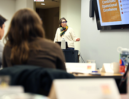 HDMZ COO Rebecca Angelos standing in front of a powerpoint presentation before a crowd of HDMZ staff at the agency summit.