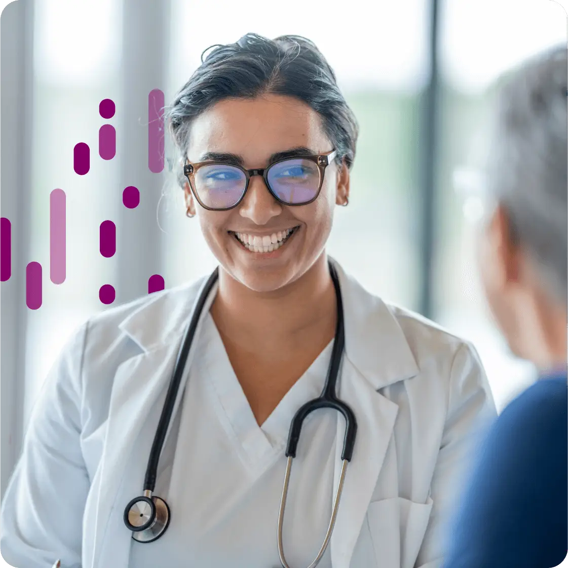 A smiling female doctor in glasses and a white coat with a stethoscope around her neck, talking to a patient.