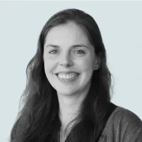 A black and white portrait of a smiling woman with long, dark hair, looking directly at the viewer.