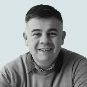 Enrique Conci headshot: A black and white headshot of a smiling man with short, dark hair, wearing a collared shirt and a sweater.